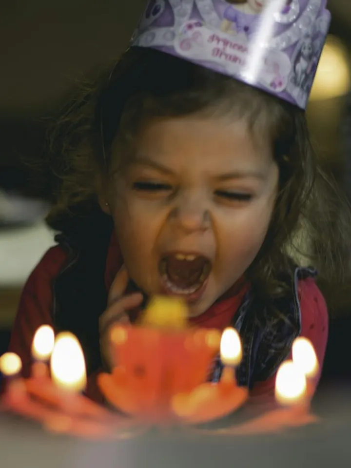 ילדה בכובע יום הולדת מול עוגה עם נרות